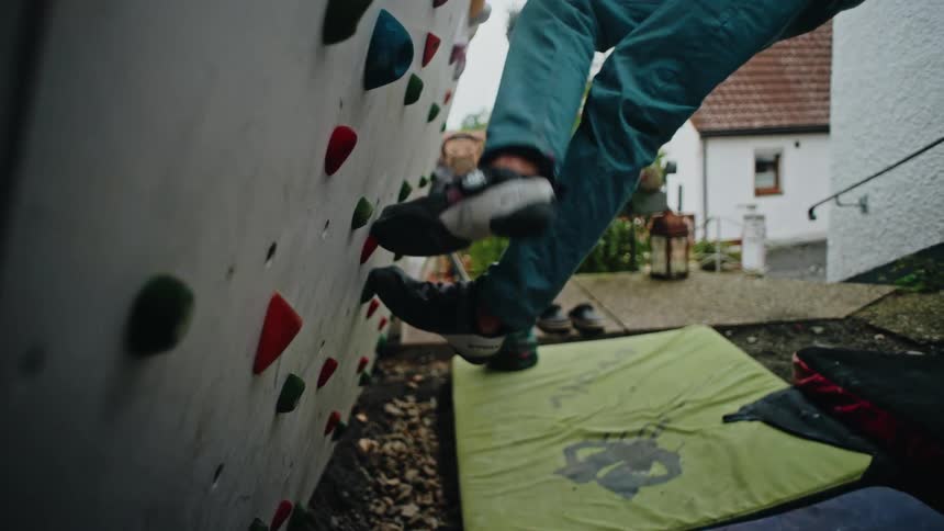 Slow motion reveal from a climber's shoe to his full body as he trains on a backyard bouldering wall