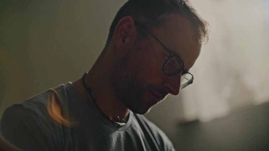 Slow-motion close-up of a contemplative man with glasses meditating peacefully in a softly lit, quiet room