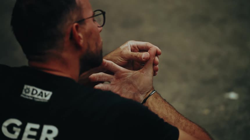 Over-the-shoulder slow motion shot of a male climber chalking his hands and stretching his fingers before a workout