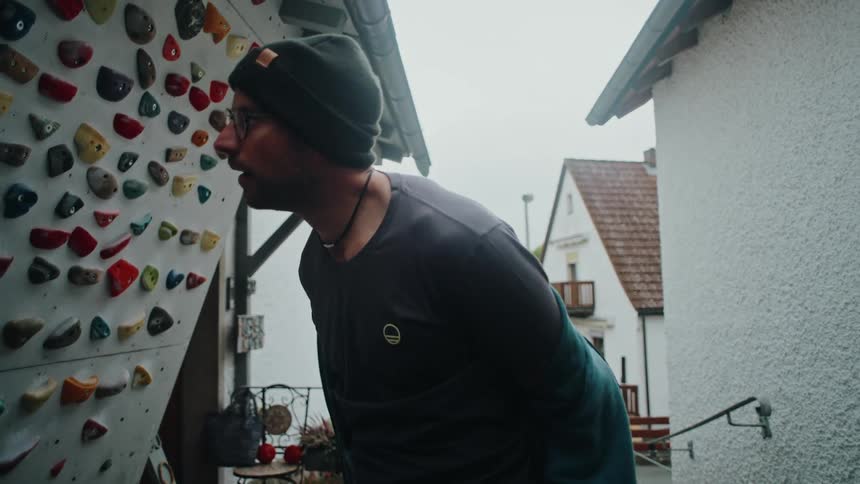A male climber takes off his hoodie in slow motion to prepare for training on his backyard bouldering wall