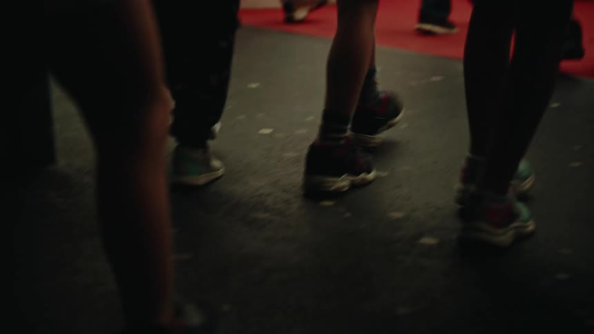 A low angle shot follows the feet of a crowd of people as they walk into a dark event space