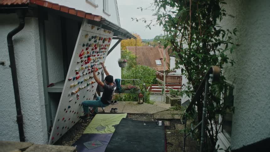 A young male athlete trains on his personal rock climbing wall in his backyard