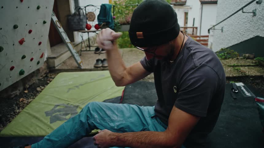 A male climber warms up in slow motion, stretching his forearms and chalking his hands before tackling his backyard bouldering wall