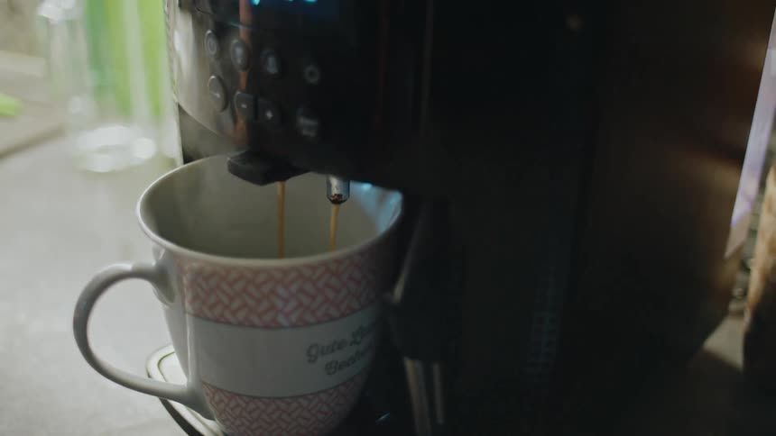An automatic espresso machine dispenses a fresh cup of steaming coffee into a white and pink mug