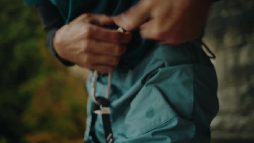 A male rock climber fastens his safety harness in slow motion, preparing for an ascent outdoors