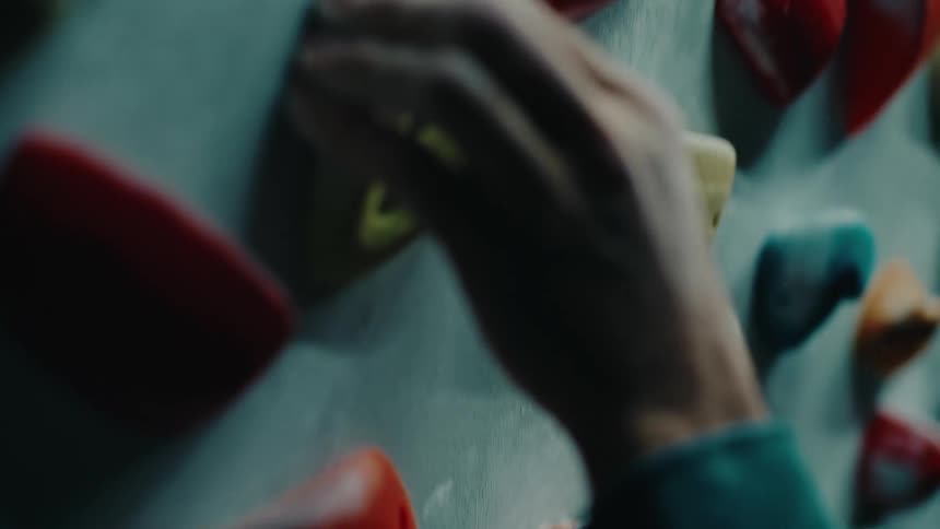 Close-up of a climber's hands carefully gripping colorful holds on an indoor bouldering wall in slow motion