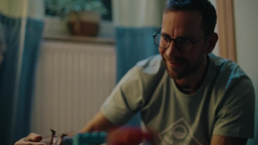 A loving father with glasses smiles and laughs while playing a board game with his child in their cozy home at night