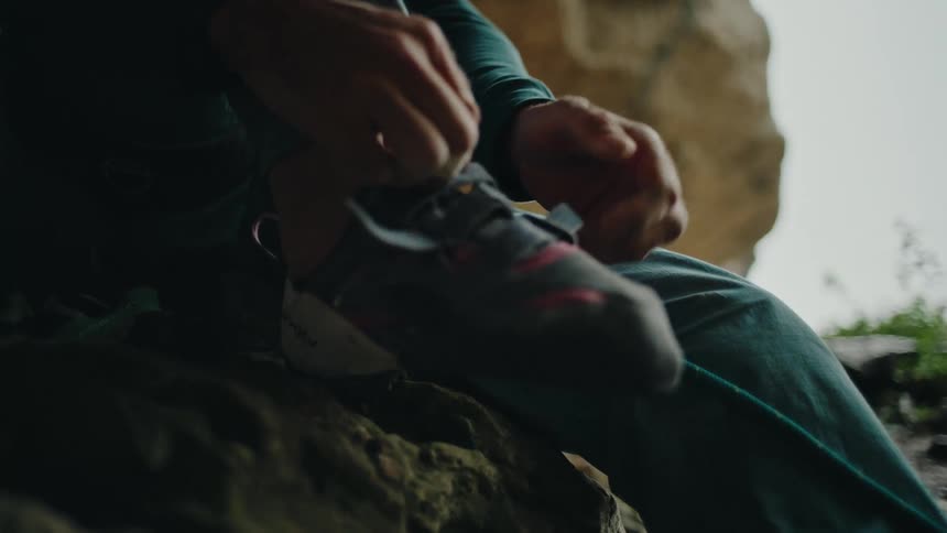 Close-up of a rock climber strapping on their climbing shoes in slow motion while preparing for a climb inside a cave