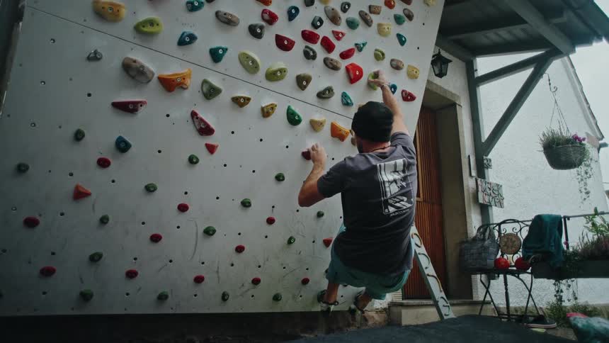 A man chalks up his hands before attempting a route on his backyard bouldering wall, ultimately falling onto the crash pad in slow motion