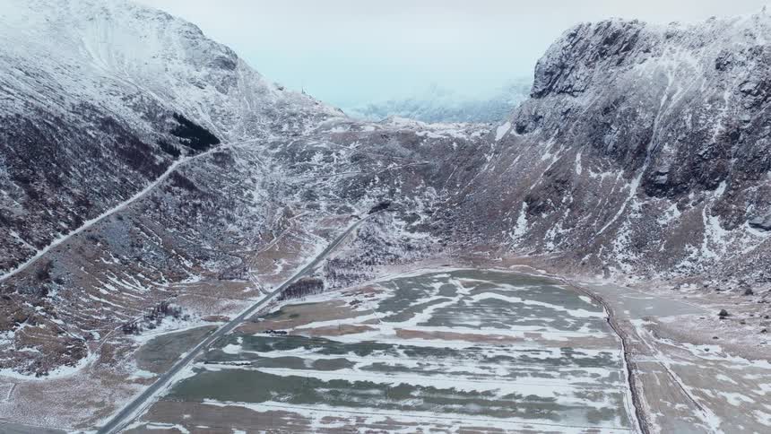 Aerial view of a snowy valley floor nestled between towering, rugged mountains in a winter landscape