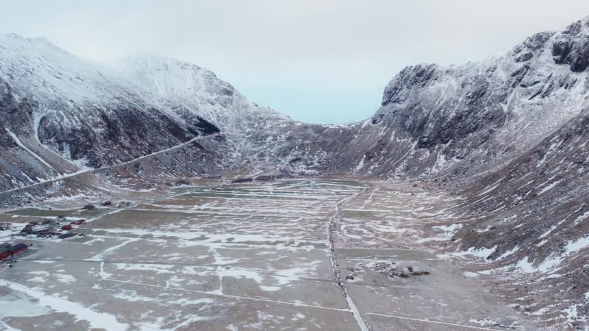 An epic aerial view slowly ascends over a vast, snow-covered valley nestled between towering mountains in Norway