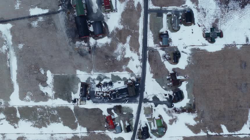 Top-down drone footage slowly rises over a small rural community and snow-covered farmland in winter