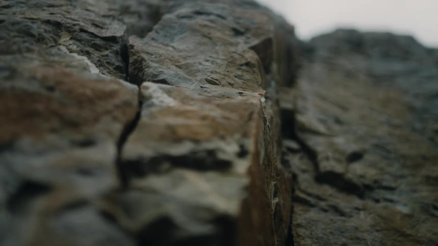 A slow, dramatic close-up pan reveals the rugged texture of a stone cliff face
