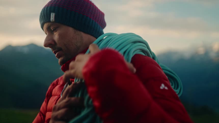 A focused male climber in a red jacket prepares his rope for an ascent in the mountains at sunrise