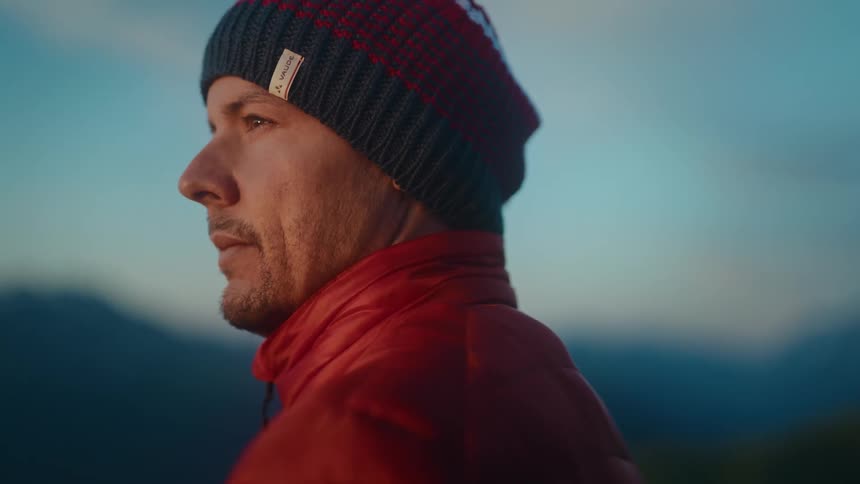 Close up of a man in a red jacket and beanie watching the sunrise in the mountains