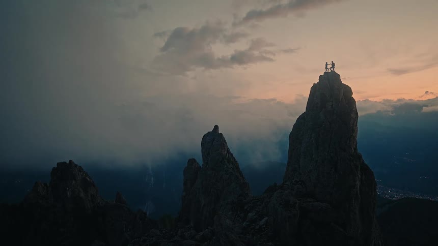 Three triumphant climbers celebrate in silhouette on a jagged mountain peak above the clouds at sunset