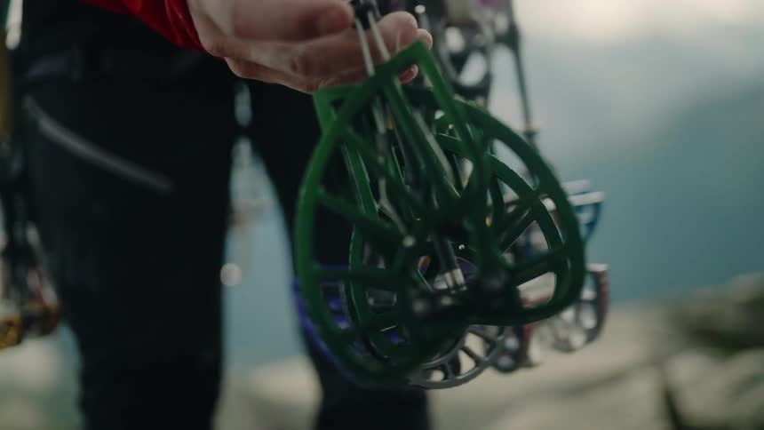 A rock climber's hand sorts through a rack of colorful spring-loaded camming devices in the mountains