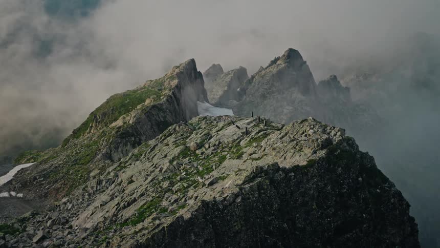 Rugged, rocky mountain peaks emerge through a thick layer of moody clouds and fog