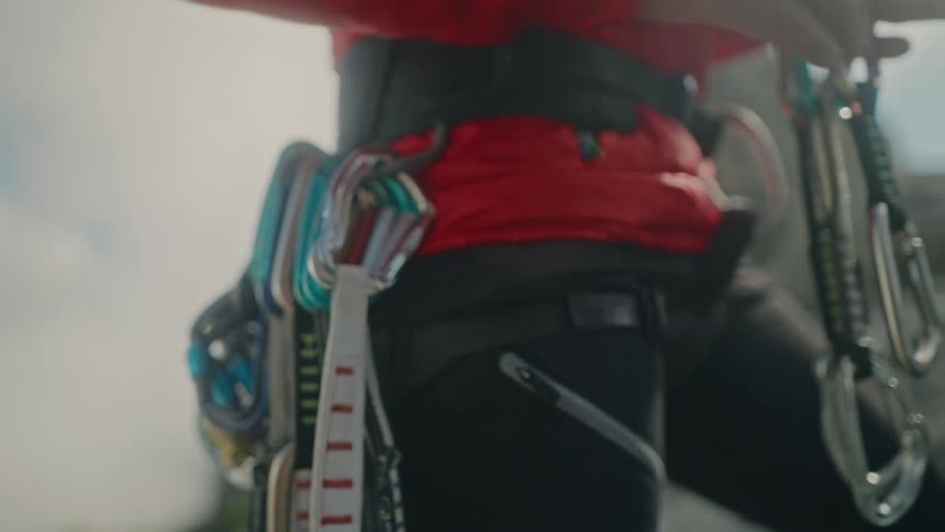 A climber meticulously organizes quickdraws and carabiners on their harness in slow motion before an ascent