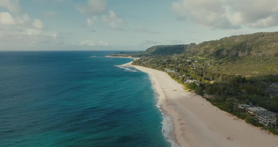A stunning wide aerial shot captures the picturesque tropical coastline, featuring a long sandy beach and vibrant turquoise ocean waters