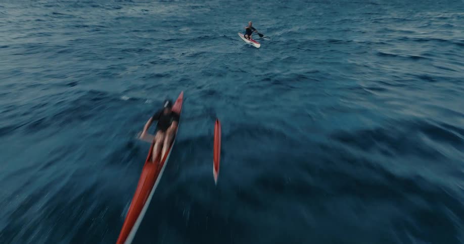 An exhilarating FPV drone shot races towards and flies over two outrigger canoe paddlers on the open sea