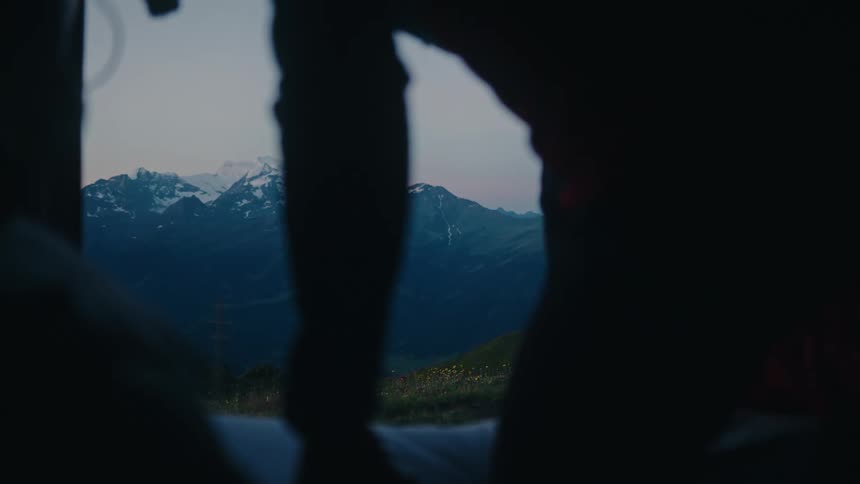 A person slowly opens the side door of a camper van, revealing a breathtaking view of snow-capped mountains at dusk