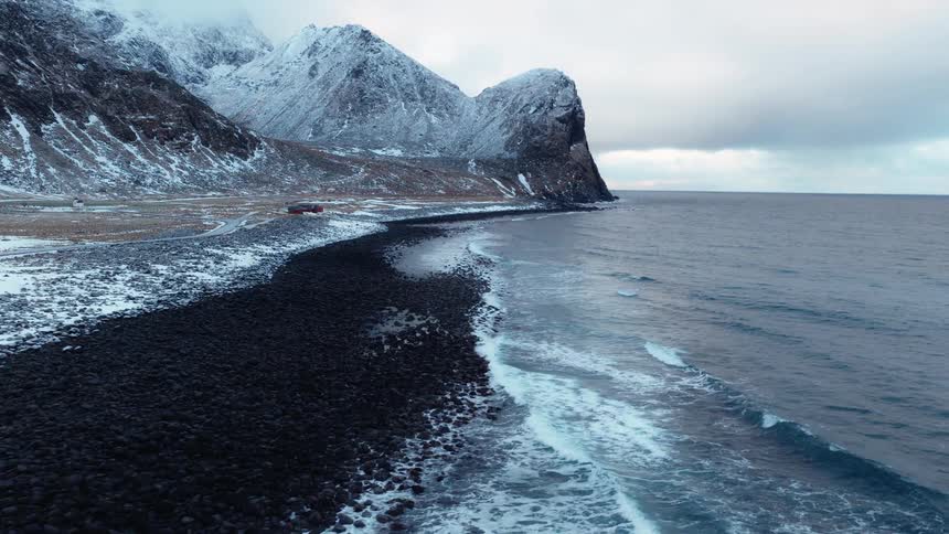 A slow aerial pullback reveals the dramatic, snow-covered coastline and mountains of Lofoten, Norway on a cold winter day