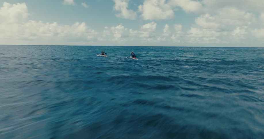 Low aerial shot follows two outrigger canoe paddlers as they move across the vast blue ocean on a beautiful day