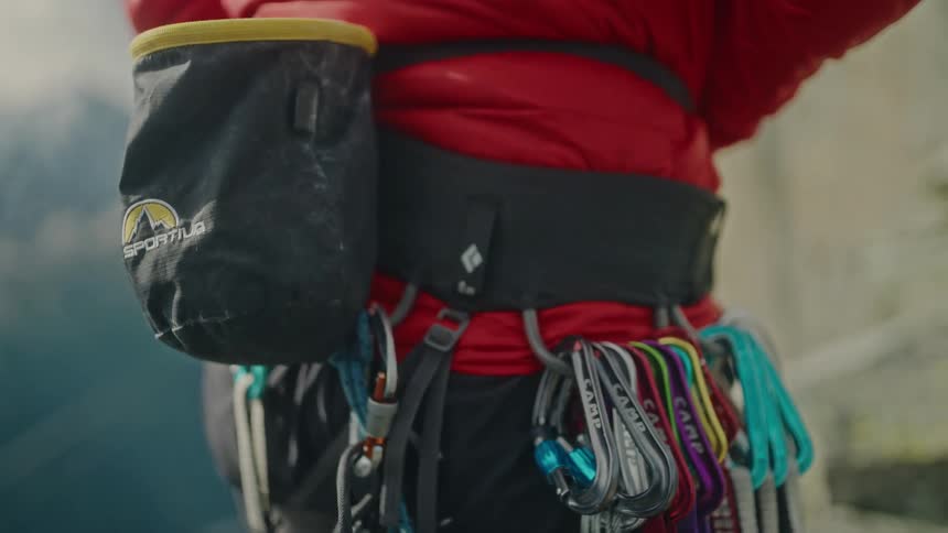 A close-up of a rock climber adjusting the strap on their chalk bag attached to a harness laden with gear