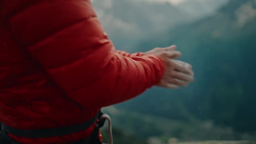 Close up of a climber wearing a harness and gear, reaching into their chalk bag and rubbing chalk on their hands in slow motion