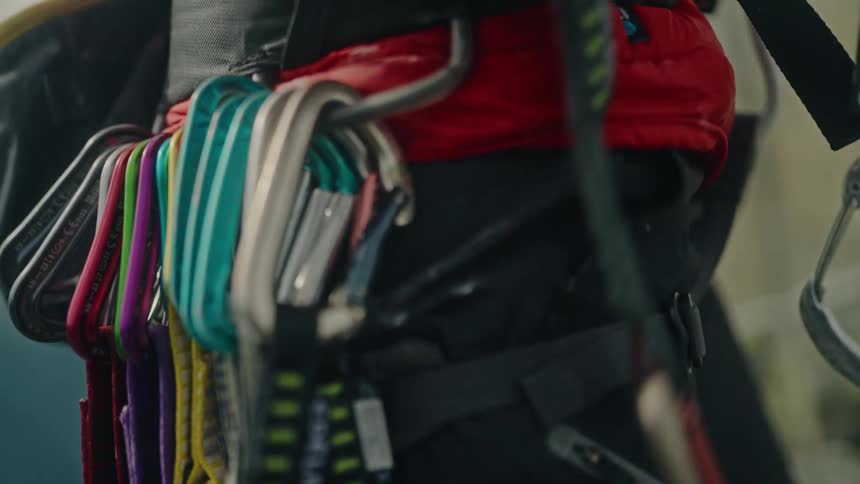 A rock climber in slow motion selects a colorful quickdraw from the gear loop on their harness before an ascent