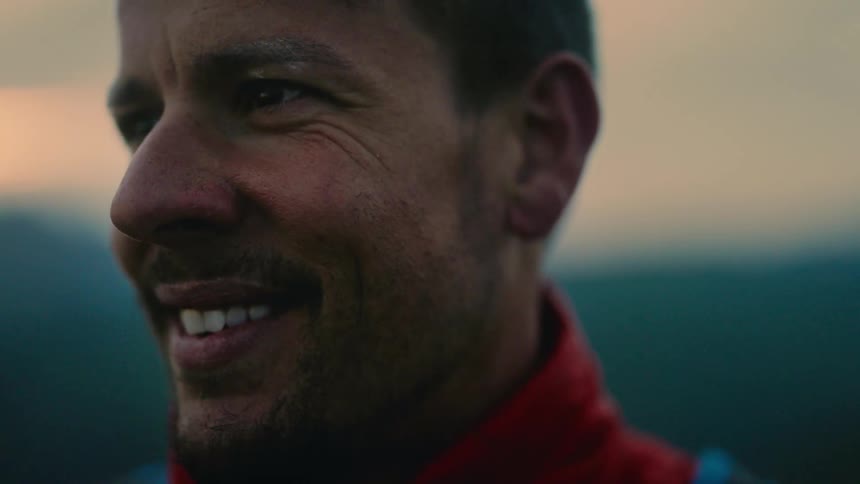 A slow focus pull reveals the smiling face of a content hiker taking in the mountain view at sunset
