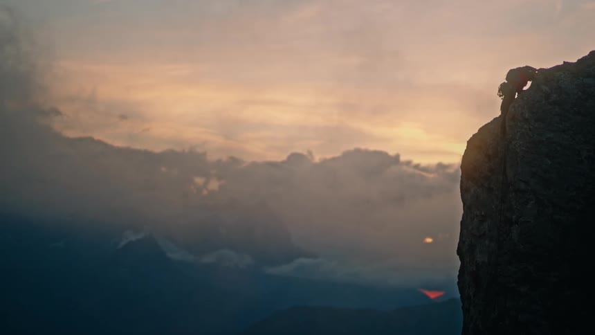 A silhouetted rock climber courageously ascends a steep mountain cliff during a breathtaking sunset