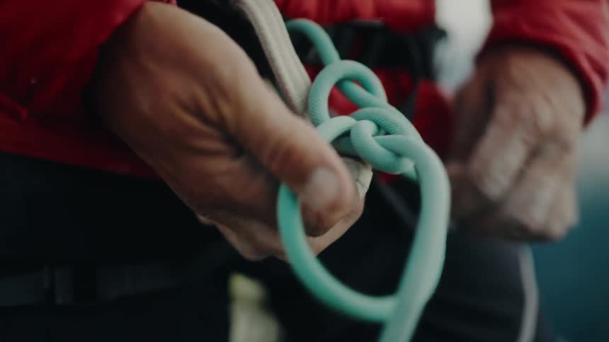 Close up of a climber's chalky hands expertly tying a figure-eight safety knot onto their harness in slow motion