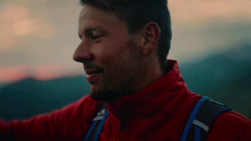 Close-up of a smiling male mountaineer taking off his helmet to enjoy the scenic mountain view at dusk