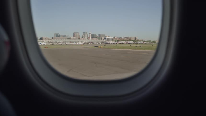A view from an airplane window shows the tarmac and a city skyline in the distance on a clear day