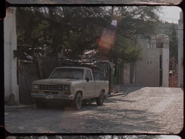 Vintage film shot of an old pickup truck parked on a quiet cobblestone street in a small town