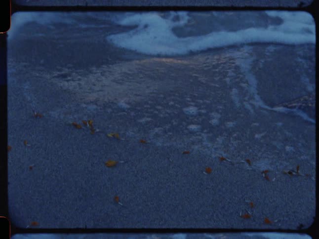 Super 8mm footage captures the gentle motion of ocean waves rolling onto a sandy shore at twilight