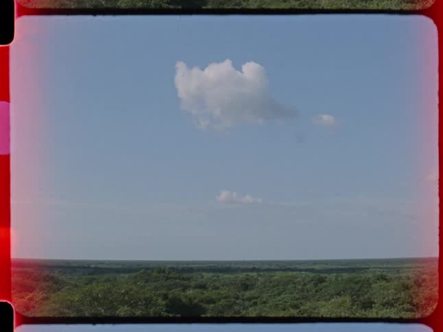 Vintage 16mm film footage shows a vast, lush green jungle landscape beneath a clear blue sky with a few small clouds