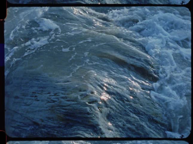 Archival 16mm film captures a powerful close-up of water churning and foaming as it rushes over rocks in a river