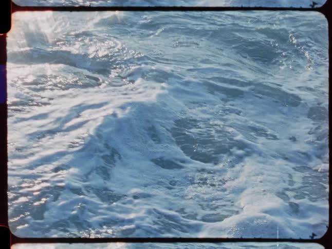 Archival footage of powerful ocean waves swirling and crashing against coastal rocks in slow motion