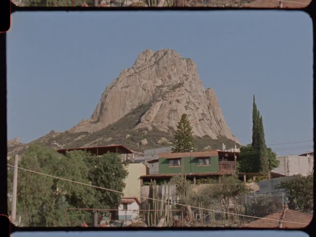 Vintage film captures a sunny day view of the iconic Peña de Bernal monolith towering over a quiet Mexican village