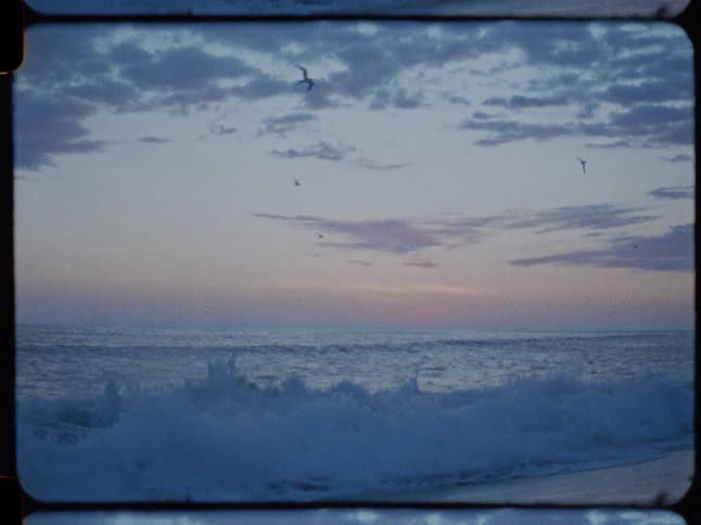 Vintage 8mm film of ocean waves crashing in slow motion with seagulls flying at twilight