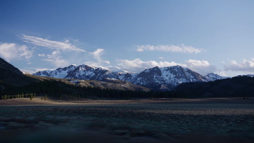 Scenic drive through a vast valley with a stunning view of a snow-covered mountain range under a clear blue sky