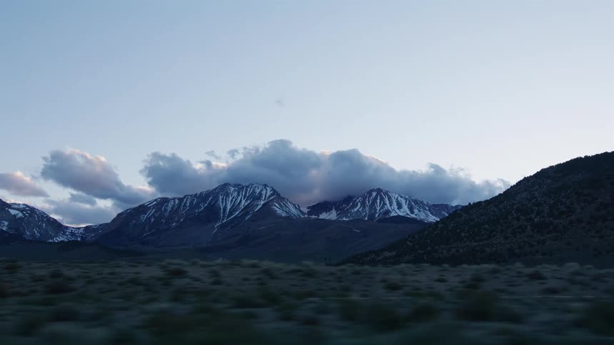 A scenic drive past majestic, snow-capped mountains shrouded in clouds at twilight