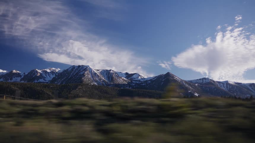 A scenic drive passing by majestic snow-capped mountains and a lush pine forest on a beautiful sunny day