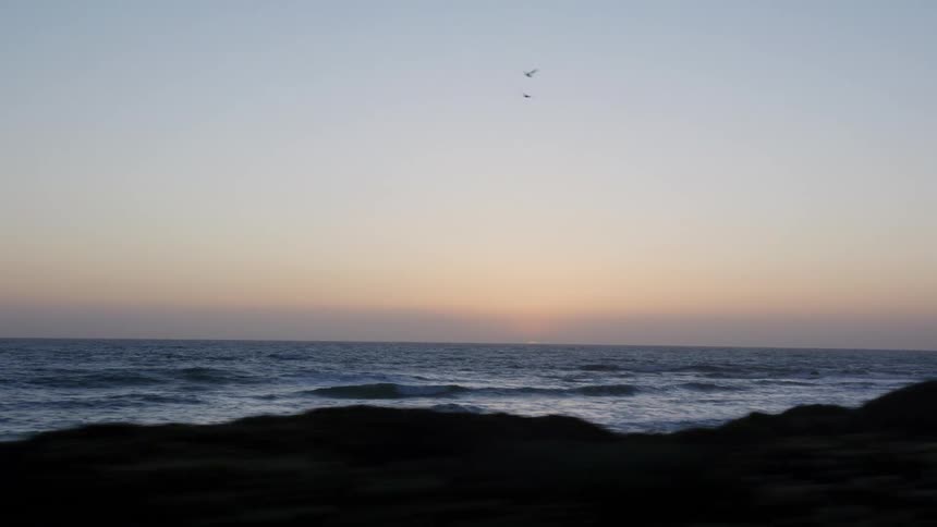 A scenic drive along the coast reveals a tranquil ocean sunset with waves gently lapping the shore