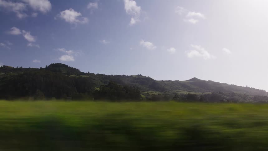 A beautiful pastoral landscape of rolling green hills and trees rushes by as seen from a moving vehicle