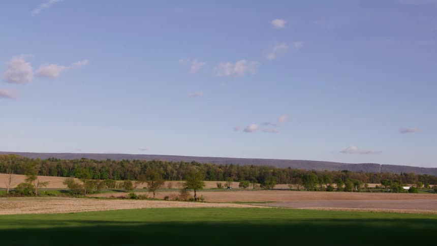 A serene, wide shot of a drone flying over a rural landscape transitions into a fast-moving side view from a vehicle