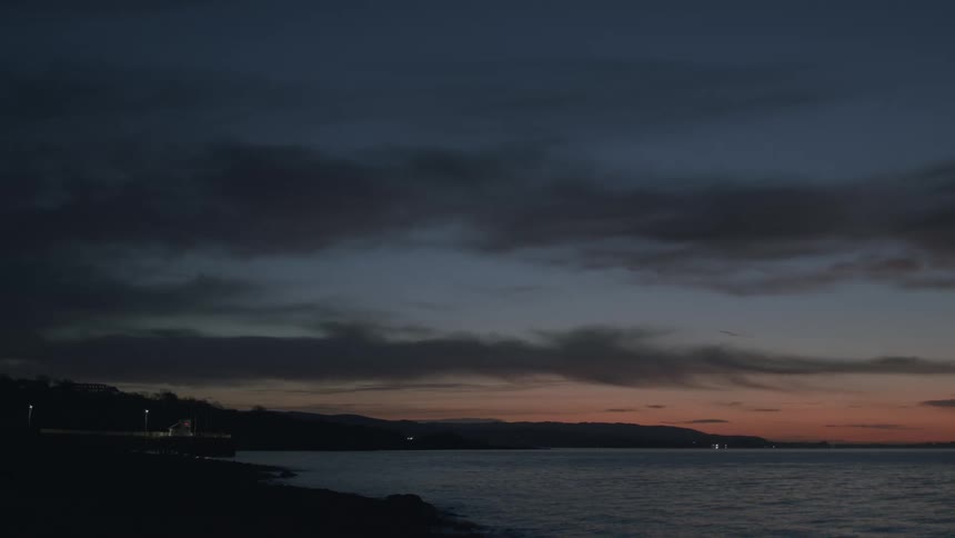 A tranquil ocean view at dusk shows the last remnants of a colorful sunset on the horizon under a dark, cloudy sky